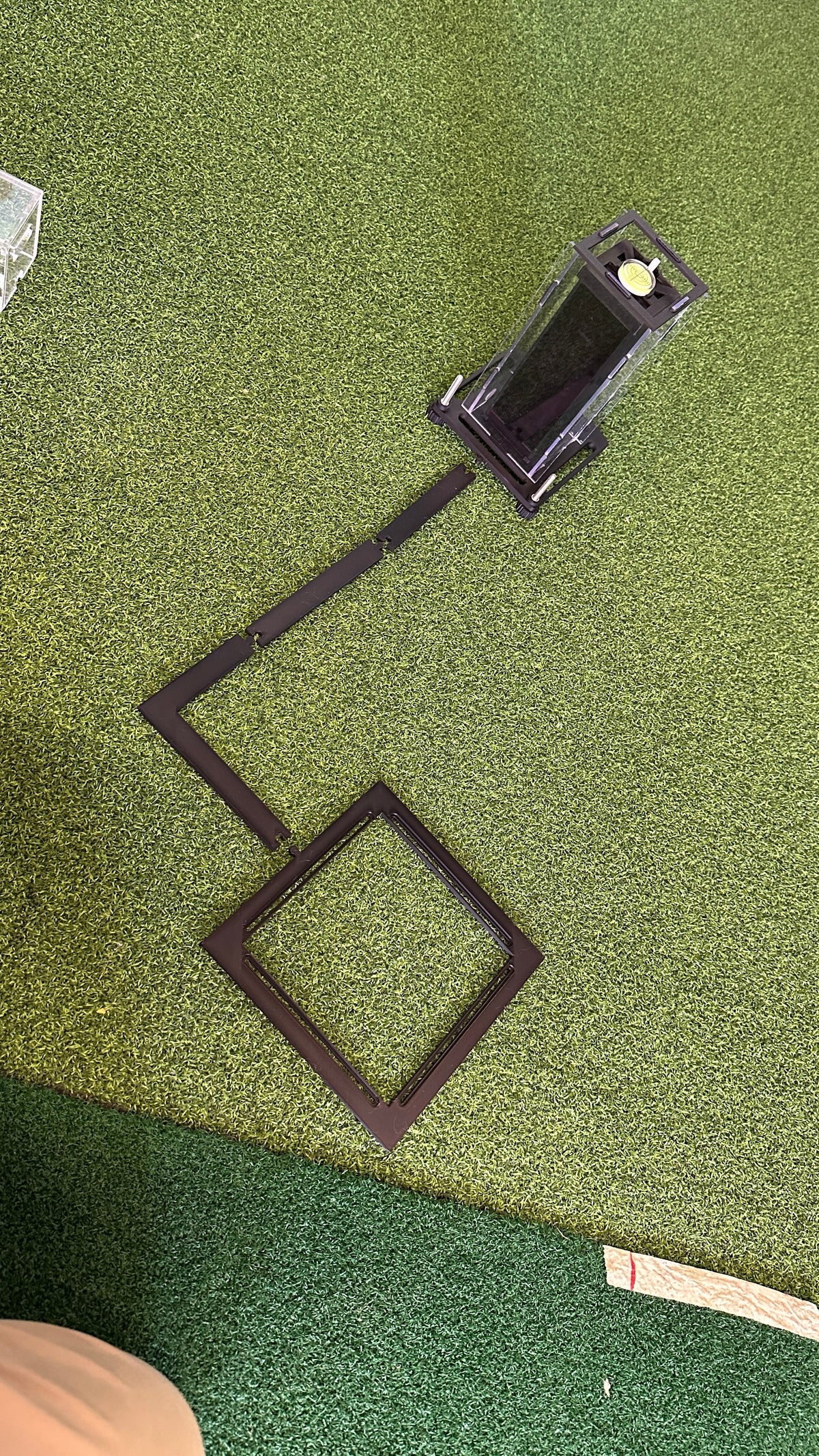 Square Golf protective case with ball positioning arm and square frame laid out on a golf mat