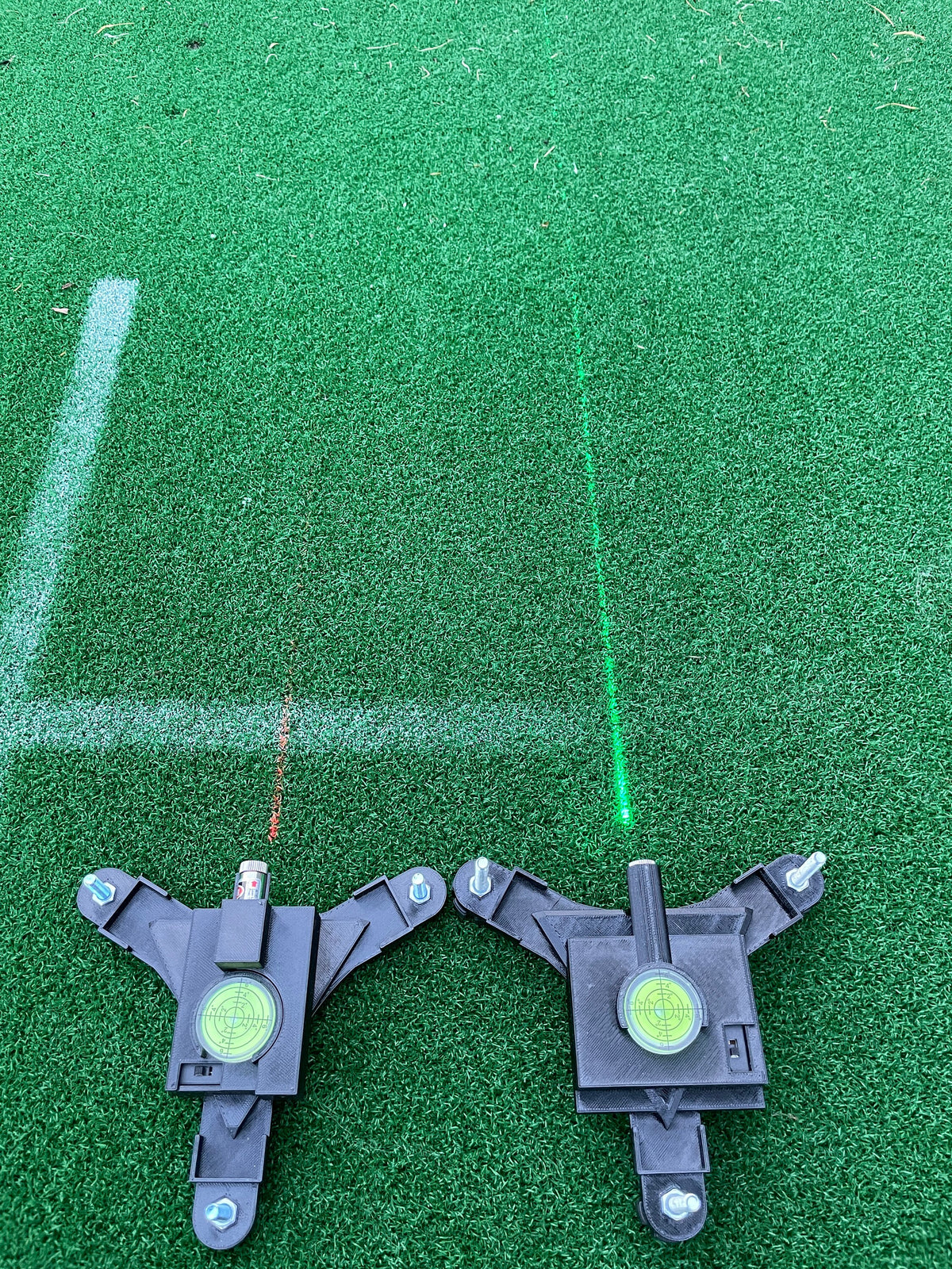 Two alignment stands projecting red and green lines onto a golf mat